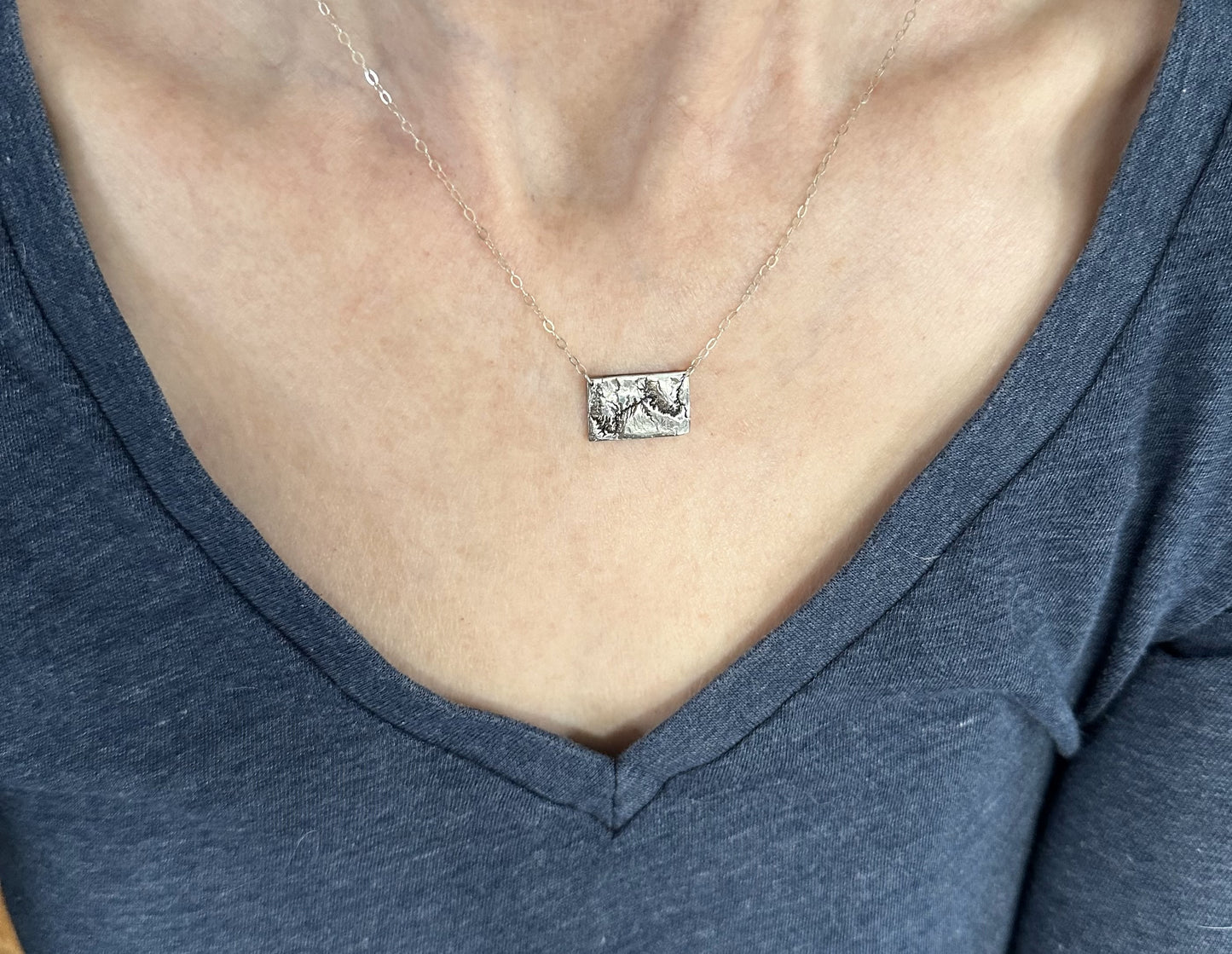 A handcrafted silver necklace showing the topographic contours of the Grand Canyon – shown on a human model