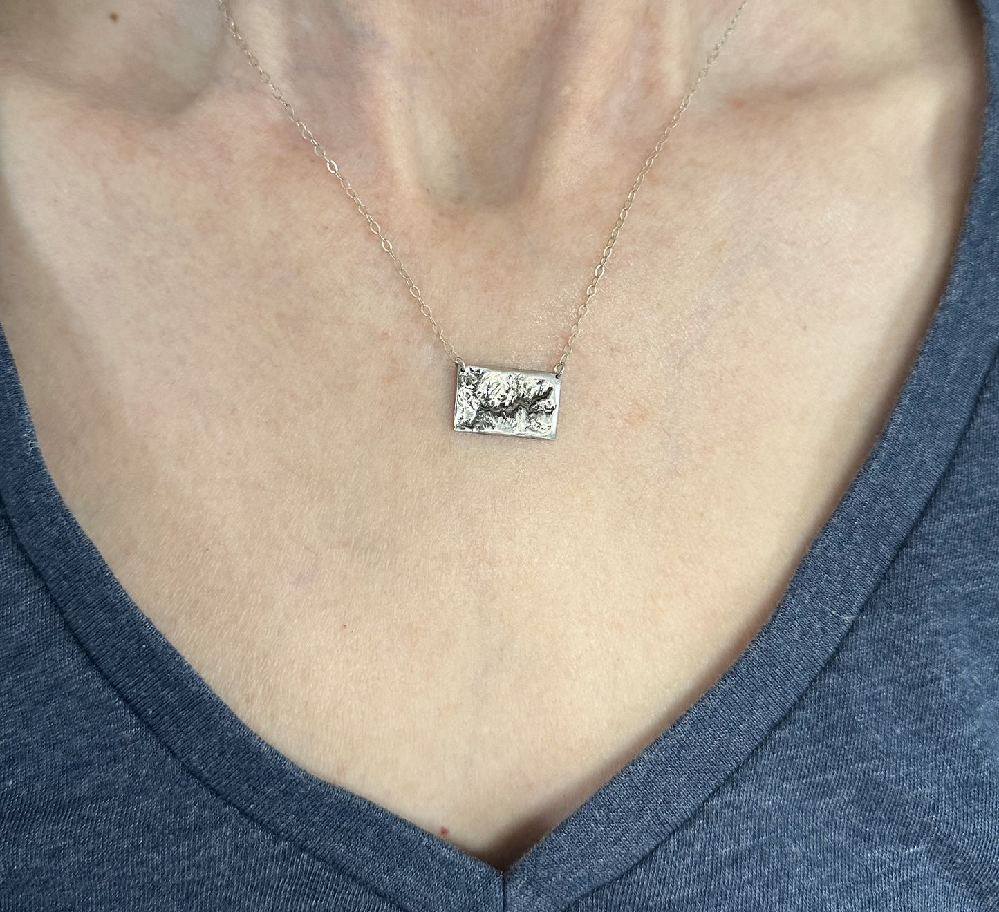 A handcrafted silver necklace showing the topographic contours of Yosemite – shown on a human model