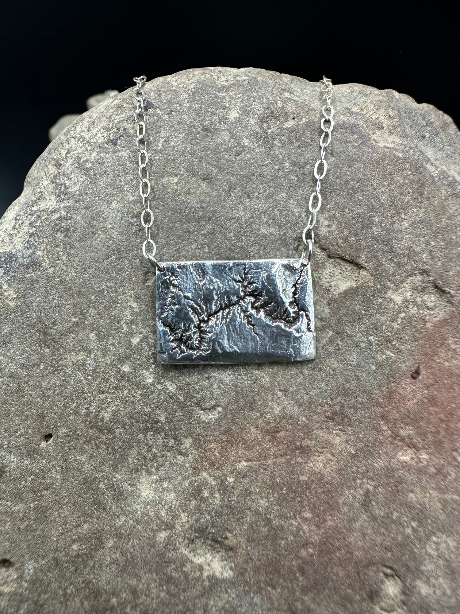 A handcrafted silver necklace showing the topographic contours of the Grand Canyon – front view