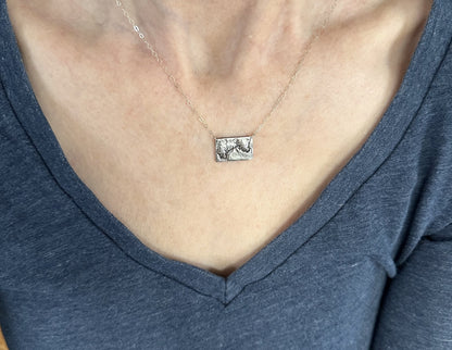 A  handcrafted silver necklace showing the topographic contours of the Grand Canyon – shown on a human model
